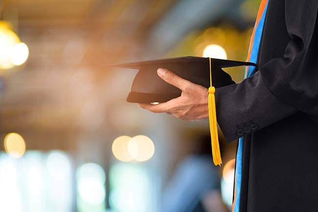 A hand holding a graduation cap with a tassle